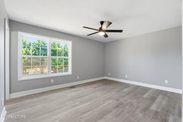 a view of an empty room with window a ceiling fan and wooden floor