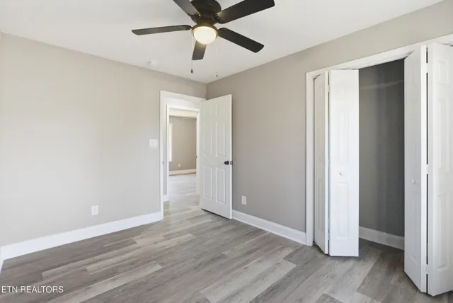 an empty room with wooden floor fan and windows