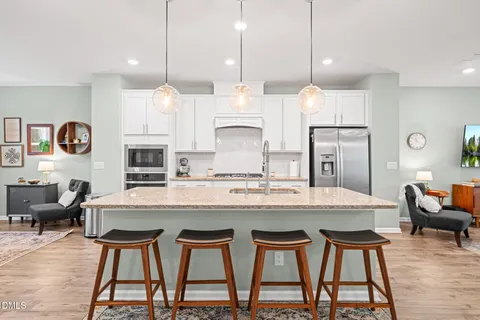 a kitchen with stainless steel appliances granite countertop a stove a refrigerator a sink a dining table and chairs with wooden floor