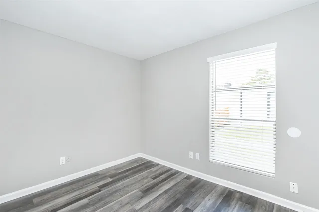 a view of an empty room with wooden floor and a window