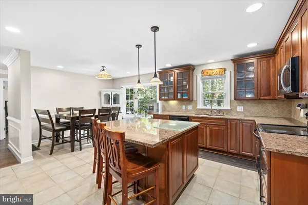 a dining hall with stainless steel appliances kitchen island granite countertop a table chairs and a sink