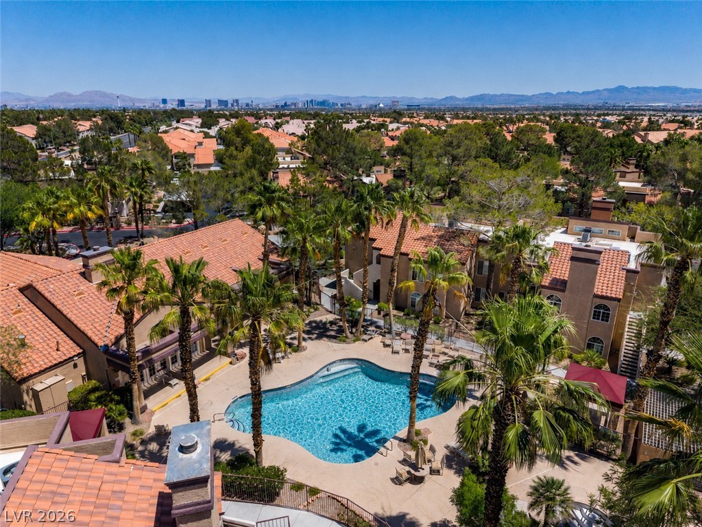 9325 West Desert Inn Road, Unit 244 Las Vegas, NV 89117 - Photo 55 of 55 An aerial perspective reveals a sparkling community pool surrounded by tropical palm trees and desert-inspired architecture, with a distant cityscape on the horizon.