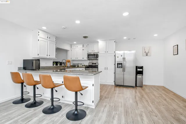 a kitchen with stainless steel appliances kitchen island granite countertop a refrigerator and a stove top oven with wooden floor