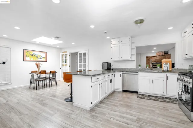 a large kitchen with granite countertop a stove top oven a sink a dining table and chairs with wooden floor