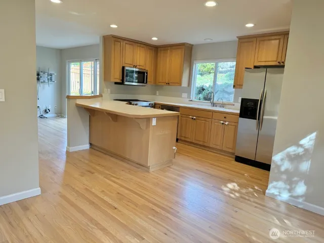 a kitchen with stainless steel appliances granite countertop a refrigerator a sink dishwasher a stove top oven a refrigerator and white cabinets with wooden floor