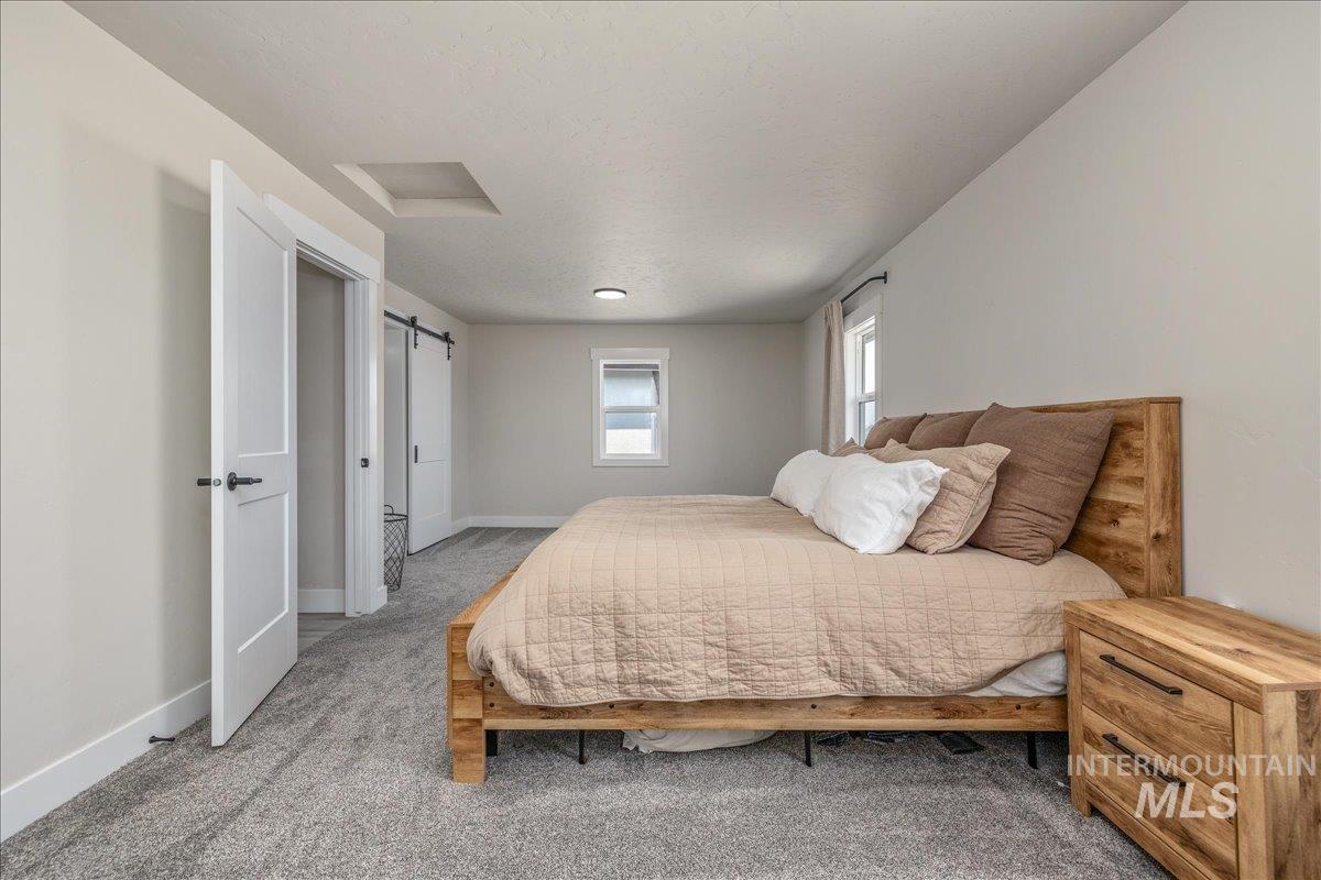 23011 Allendale Road Parma, ID 83660 - Photo 19 of 50 Carpeted flooring, vaulted ceiling, white walls, and a sliding barn door leading to an attached bathroom featuring a double vanity with matte black fixtures