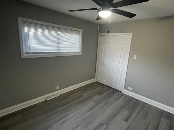 an empty room with wooden floor fan and windows