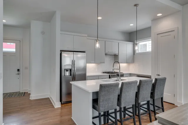 a kitchen with stainless steel appliances granite countertop a dining table chairs refrigerator and microwave