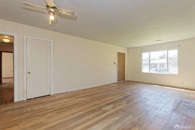 an empty room with wooden floor chandelier fan and windows