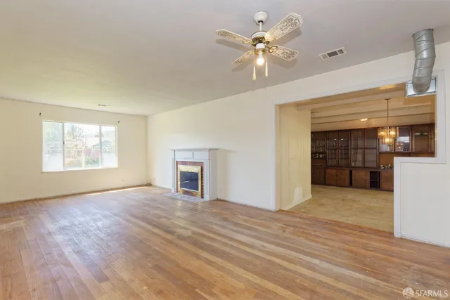 an empty room with wooden floor chandelier fan and windows