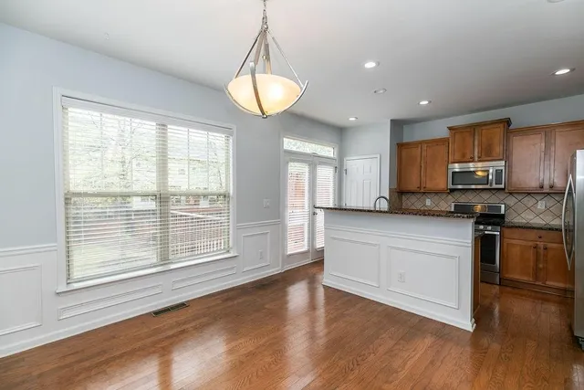 a kitchen with stainless steel appliances granite countertop a stove a refrigerator a sink a microwave oven with white cabinets and wooden floor