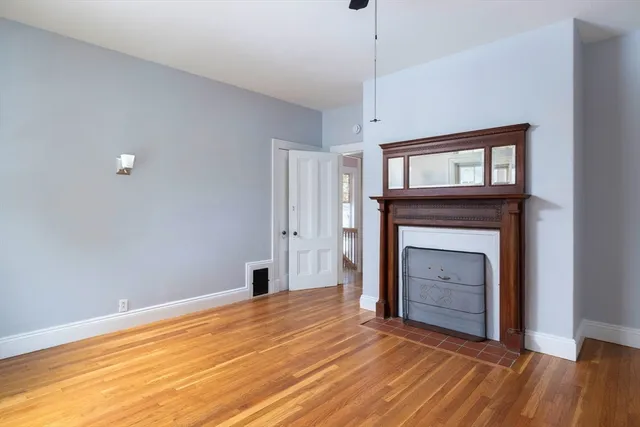 a view of an empty room with wooden floor fireplace and a window
