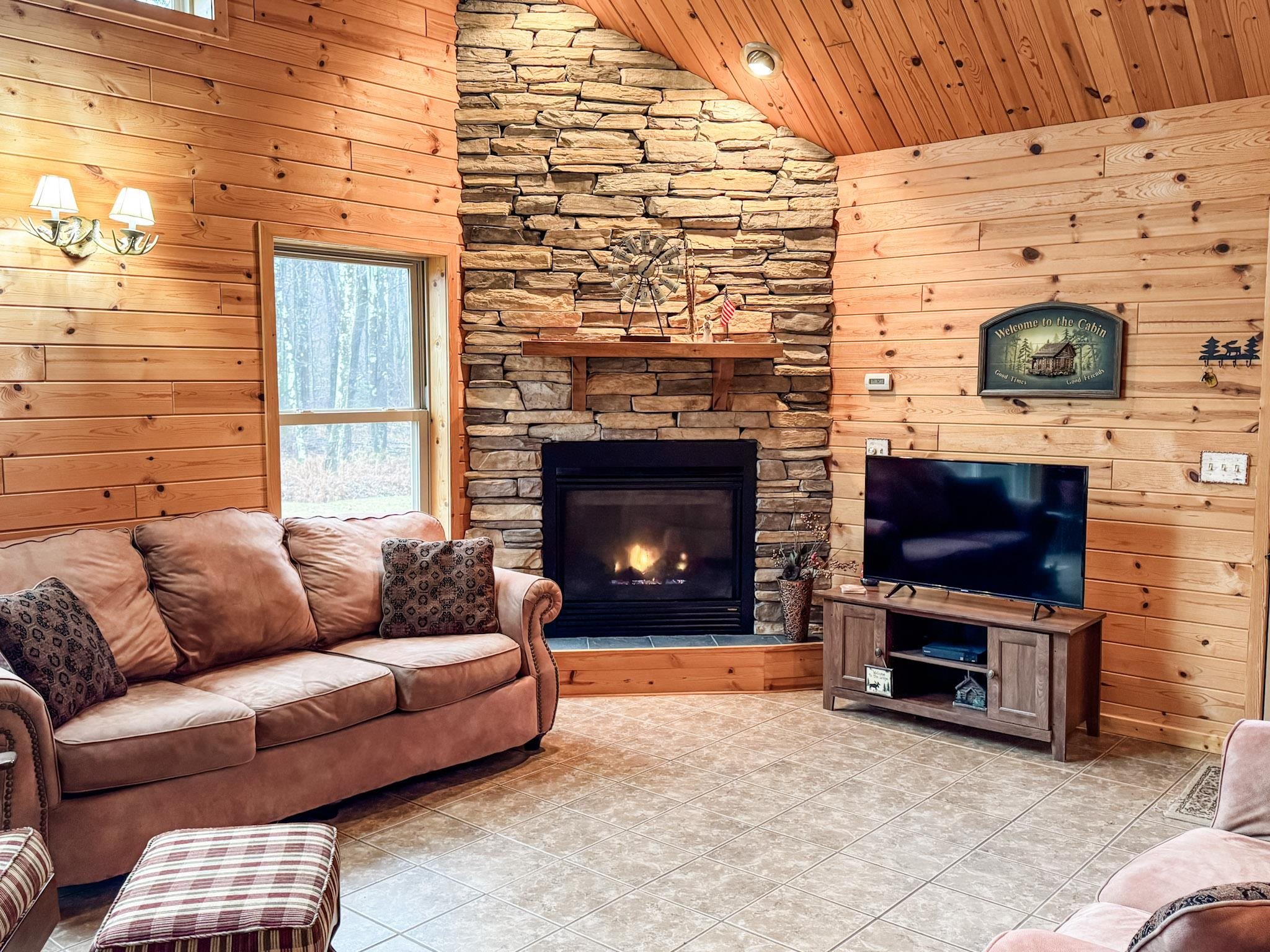 11466 Westerlund Loop Solon Springs, WI 54873 - Photo 13 of 55 Tiled living area with lofted ceiling, wood walls, healthy amount of natural light, wood ceiling, and a stone fireplace