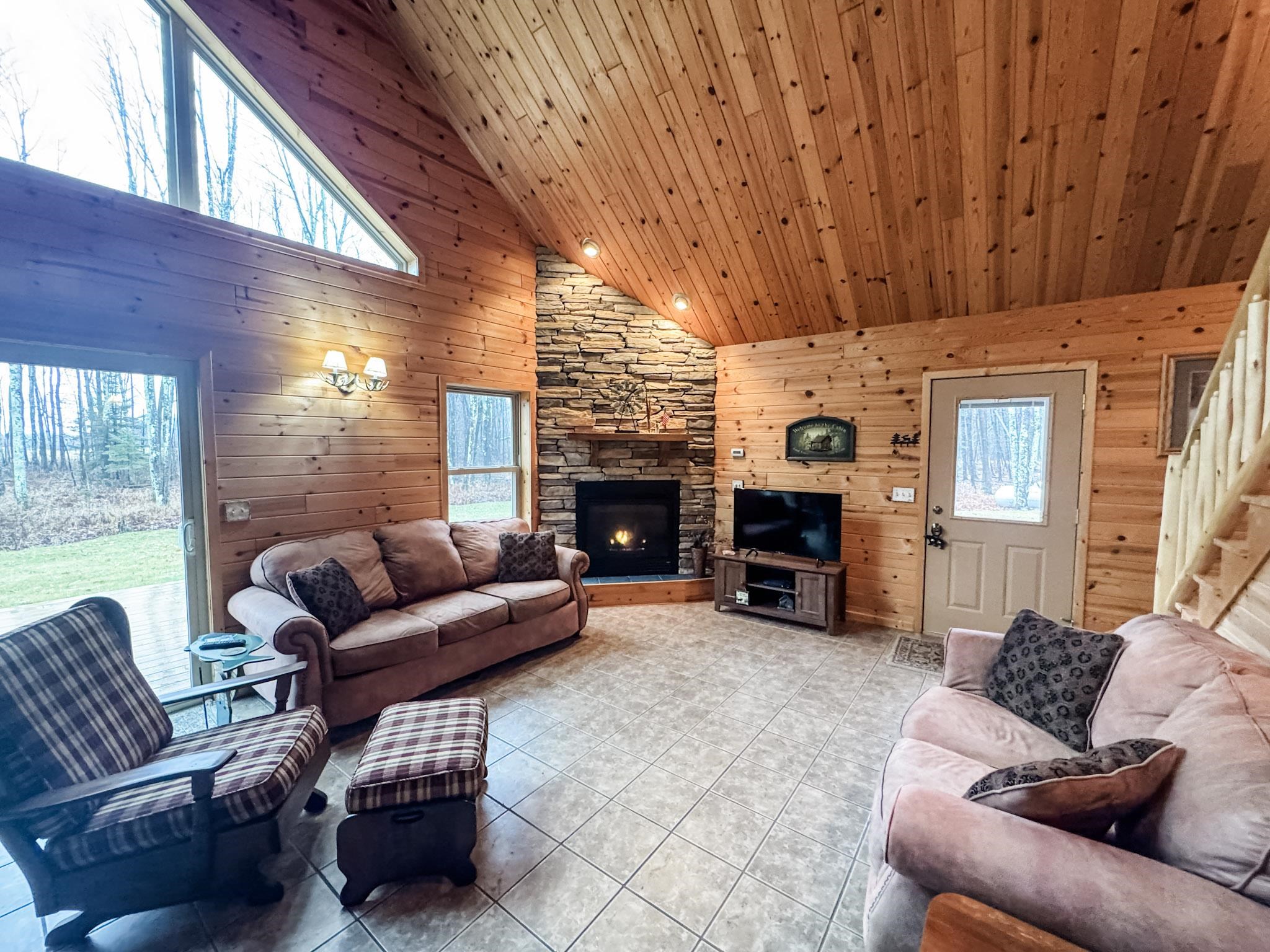 11466 Westerlund Loop Solon Springs, WI 54873 - Photo 14 of 55 Tiled living area featuring high vaulted ceiling, plenty of natural light, wood walls, a stone fireplace, and wood ceiling