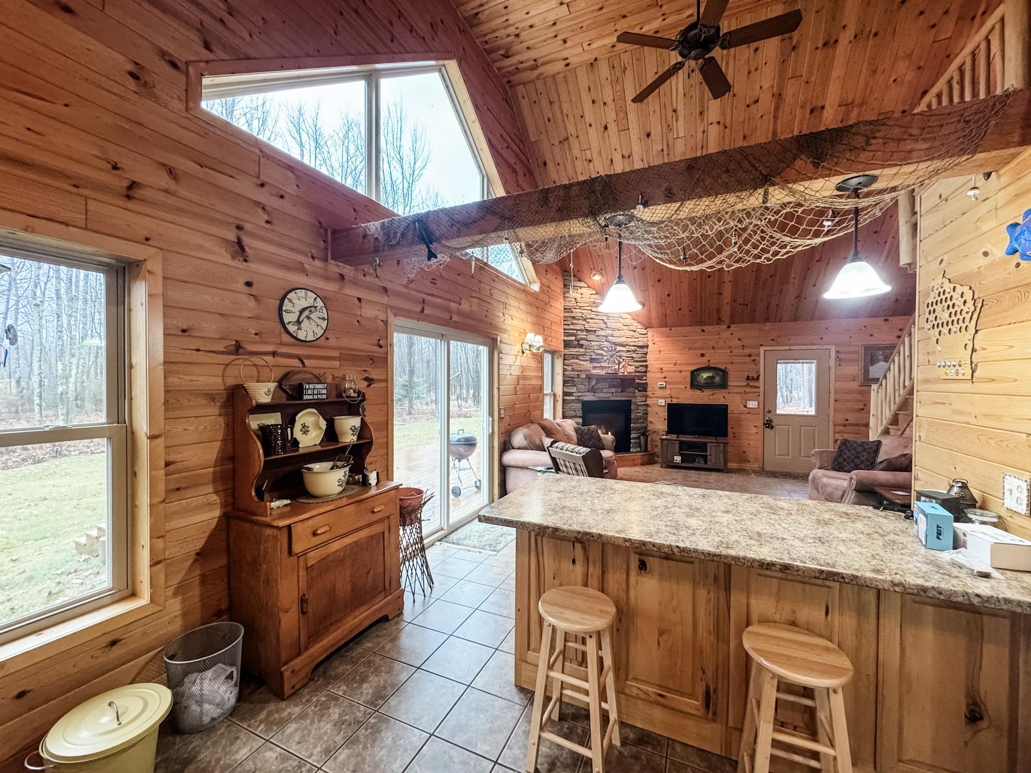 11466 Westerlund Loop Solon Springs, WI 54873 - Photo 15 of 55 Kitchen featuring wood walls, high vaulted ceiling, a stone fireplace, ceiling fan, and light tile patterned flooring