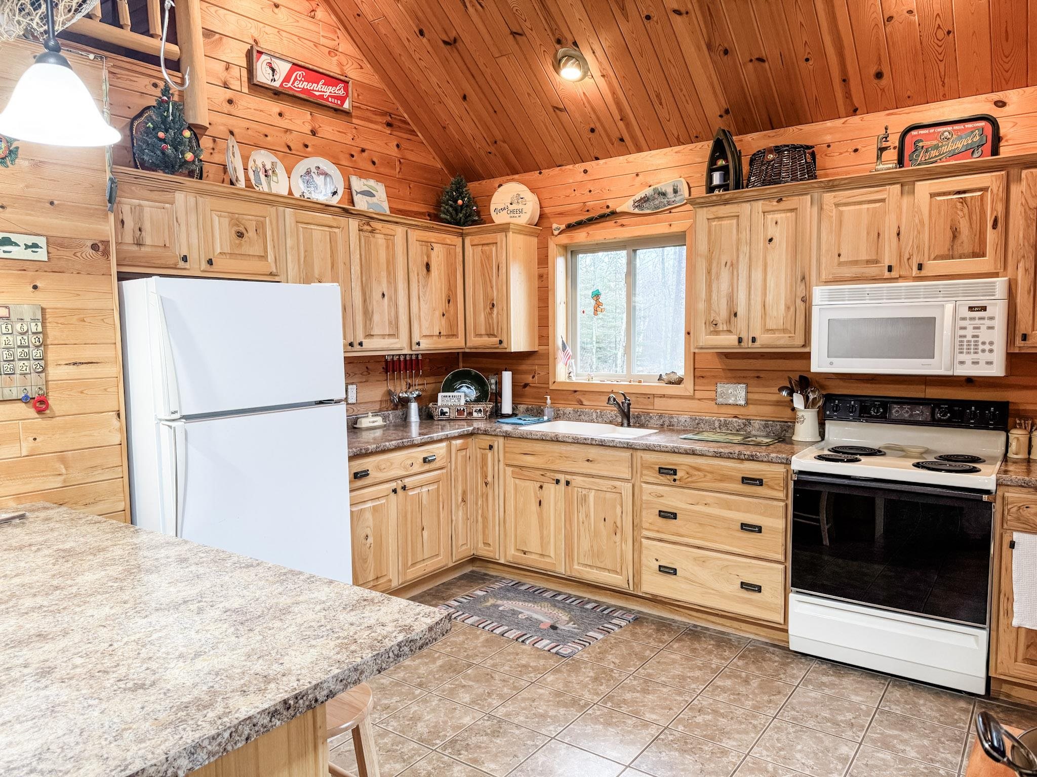 11466 Westerlund Loop Solon Springs, WI 54873 - Photo 18 of 55 Kitchen with wood walls, white appliances, vaulted ceiling, wood ceiling, and light brown cabinetry