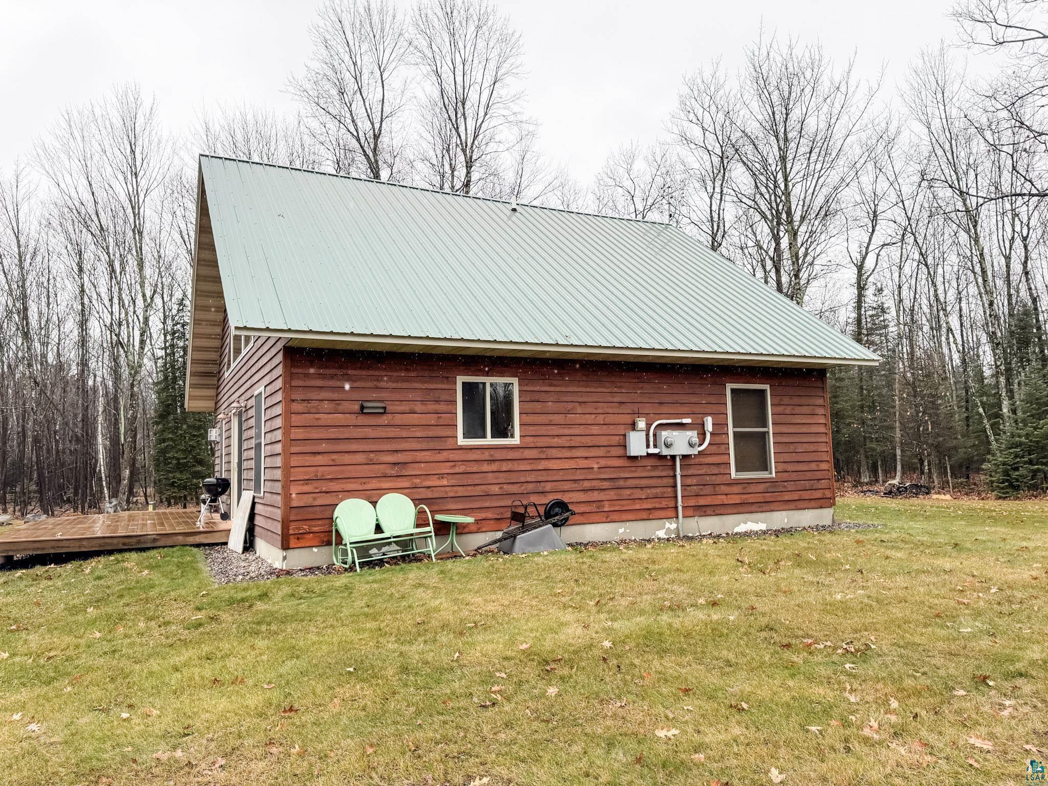View of property exterior featuring a yard, a wooden deck, and a metal roof