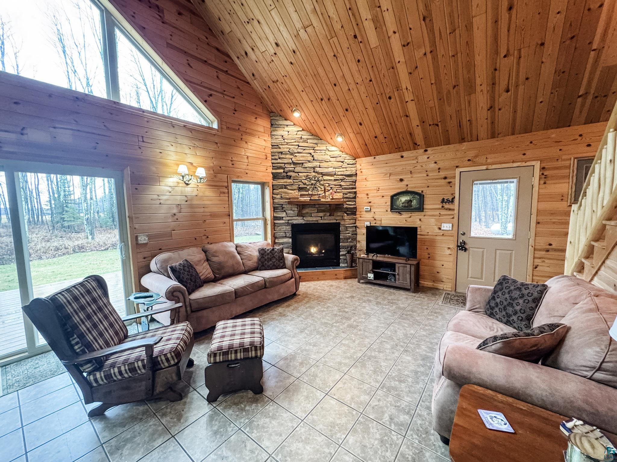 11466 Westerlund Loop Solon Springs, WI 54873 - Photo 10 of 55 Tiled living room with high vaulted ceiling, wooden walls, a stone fireplace, and wooden ceiling