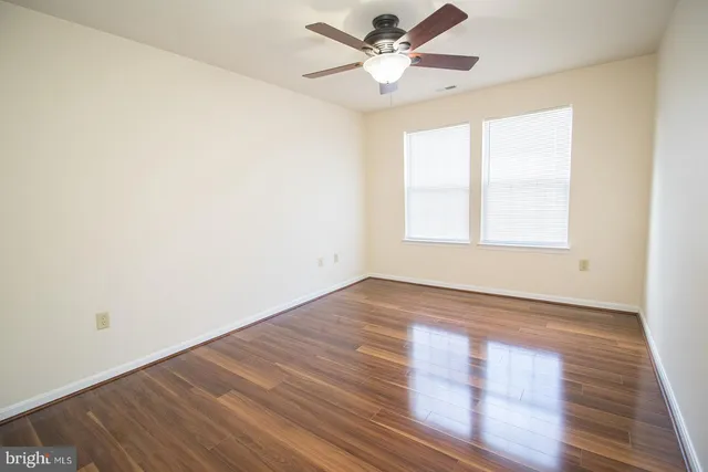 an empty room with wooden floor fan and windows
