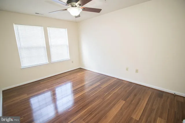 an empty room with wooden floor fan and windows