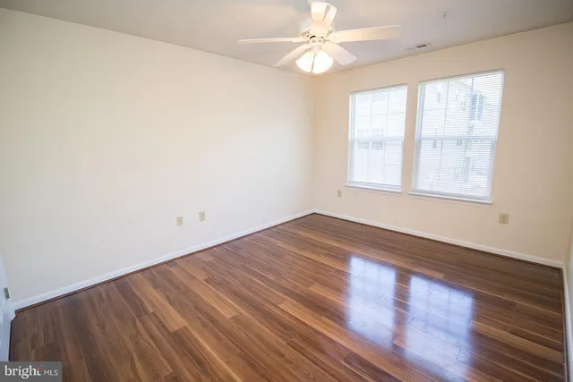 an empty room with wooden floor fan and windows