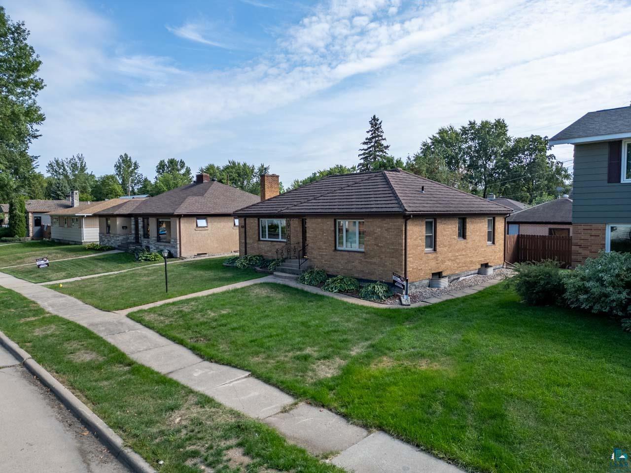 716 South 9th Street Virginia, MN 55792 - Photo 36 of 43 Brick exterior with a brown shingle roof, established landscaping, and a concrete sidewalk