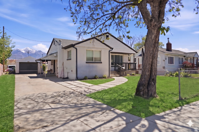 7879 Oak Street Midvale, UT 84047 - Photo 2 of 32 White exterior residence featuring a front yard with manicured lawn, a paved driveway, and a detached garage