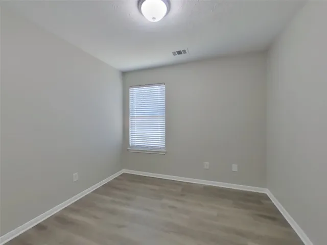 a view of an empty room with wooden floor and window