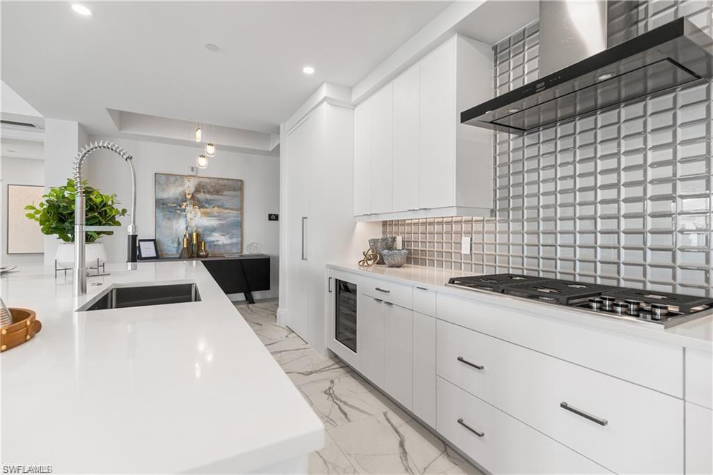 1130 3rd Avenue South, Unit 410 Avon Park, FL 33825 - Photo 17 of 21 Kitchen with wall chimney exhaust hood, stainless steel gas cooktop, sink, decorative backsplash, and white cabinets