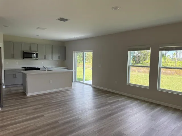 a view of a kitchen and an empty room with wooden floor and a window