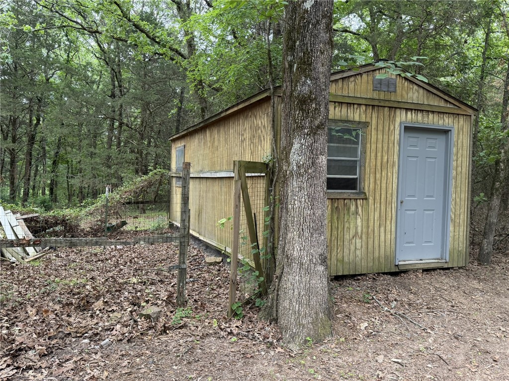 5108 Ridge Road Alma, AR 72921 - Photo 32 of 33 Wood-sided outbuilding with a gray paneled door and window, situated among mature trees