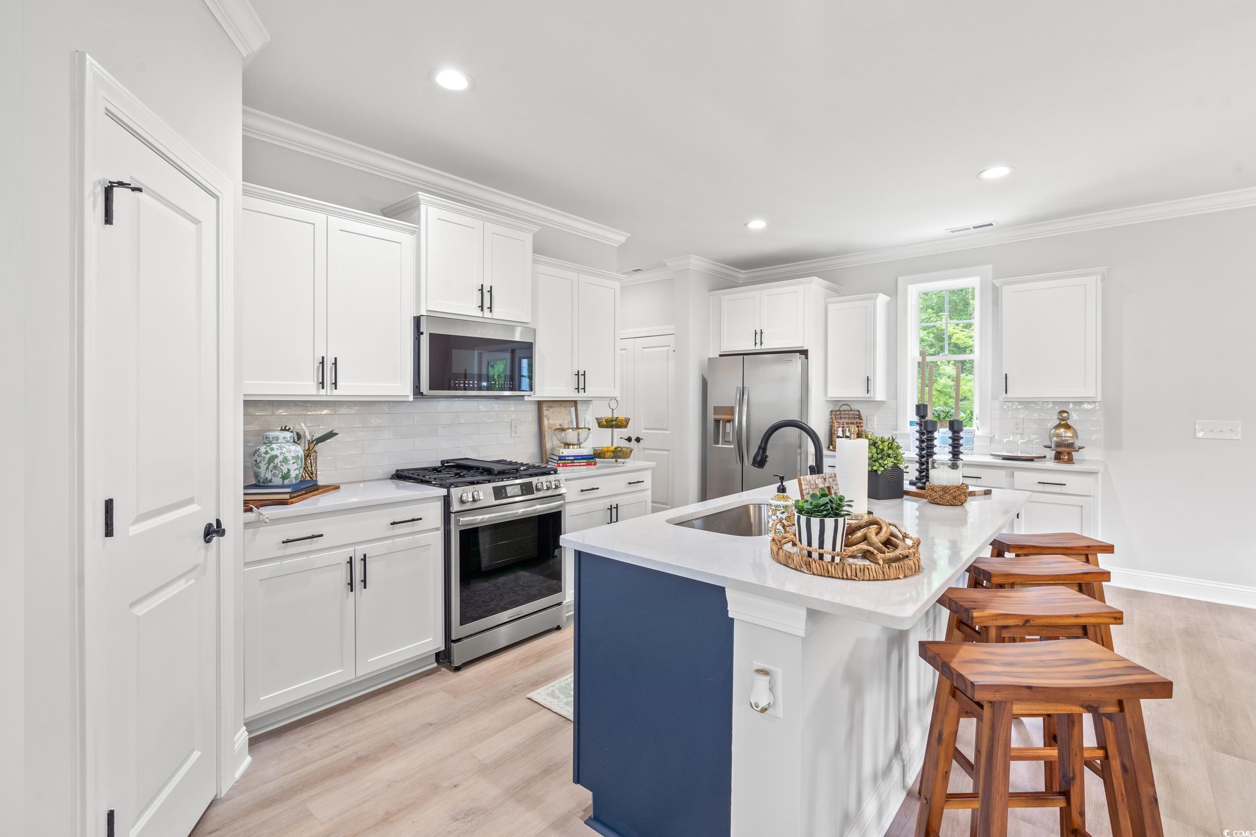 852 Commanders Island Road Georgetown, SC 29440 - Photo 6 of 37 Kitchen with stainless steel appliances, a sink, light wood-style flooring, a kitchen island with sink, and light countertops