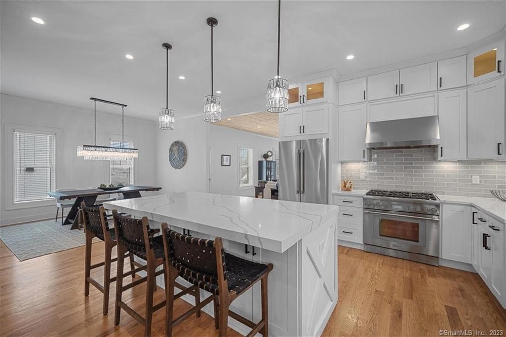 a large kitchen with stainless steel appliances granite countertop a stove a refrigerator a oven a sink a dining table and chairs with wooden floor