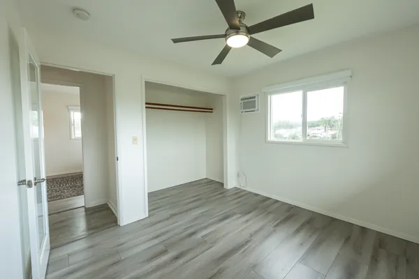 an empty room with wooden floor fan and windows