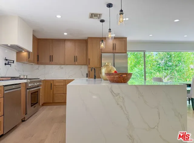 a kitchen with kitchen island granite countertop a stove a sink a refrigerator and blue cabinets with wooden floor