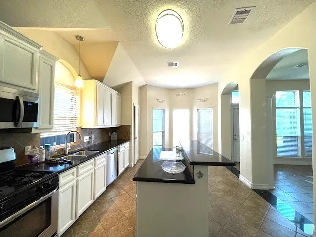 a view of a kitchen with kitchen island granite countertop a large window cabinets and stainless steel appliances
