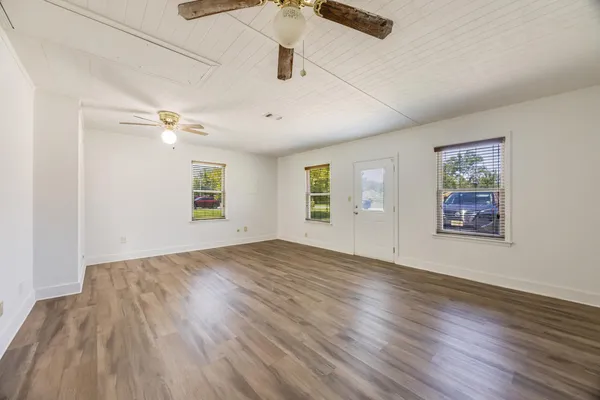 an empty room with wooden floor chandelier fan and windows
