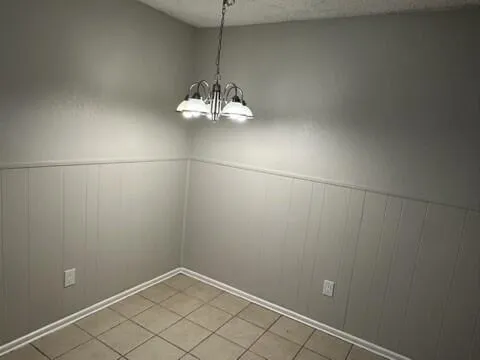 an empty room with chandelier fan and kitchen view