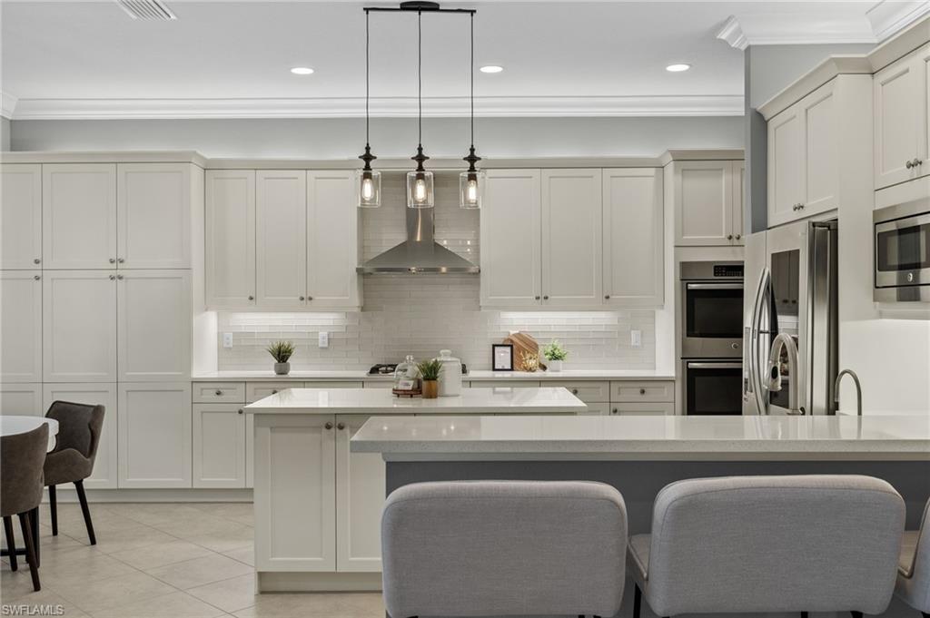 4398 Caldera Circle Naples, FL 34119 - Photo 11 of 50 a kitchen with stainless steel appliances granite countertop a sink a stove a refrigerator and white cabinets with wooden floor
