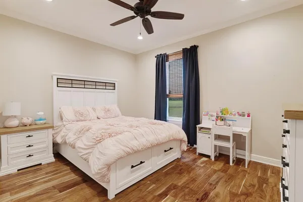 a bedroom with a bed a desk and chair with wooden floor
