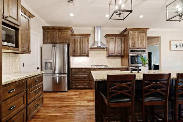 a kitchen with stainless steel appliances granite countertop a refrigerator a stove a sink a dining table and chairs with wooden floor