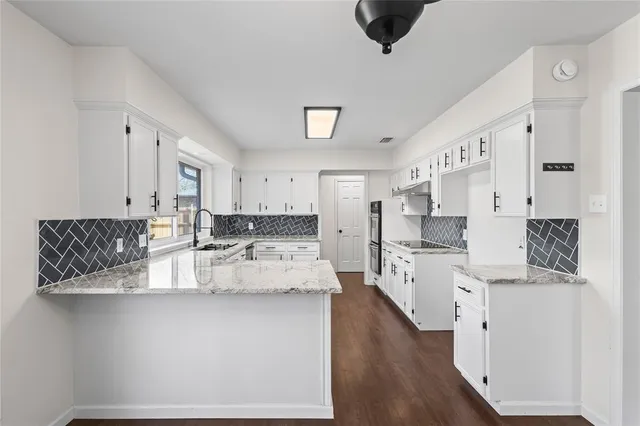 a large white kitchen with stainless steel appliances granite countertop a stove a sink dishwasher and a refrigerator with wooden floor