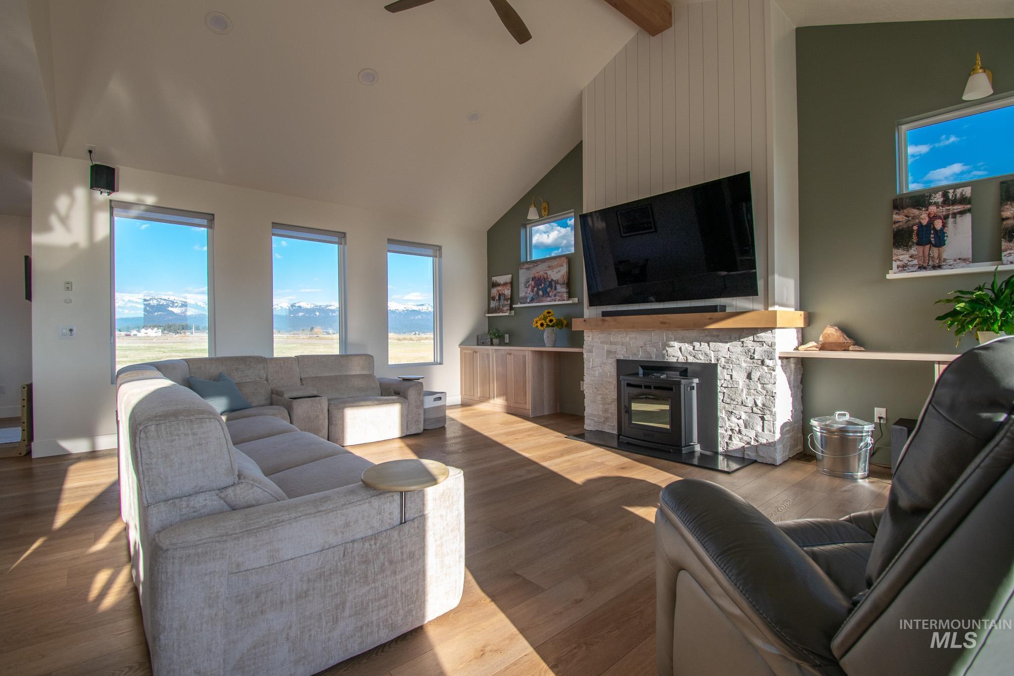 44 Big Moose Road McCall, ID 83638 - Photo 15 of 50 Living area featuring vaulted ceilings, wood-finish flooring, a stone-clad fireplace with a wood mantle, and three horizontal windows with mountain scenery