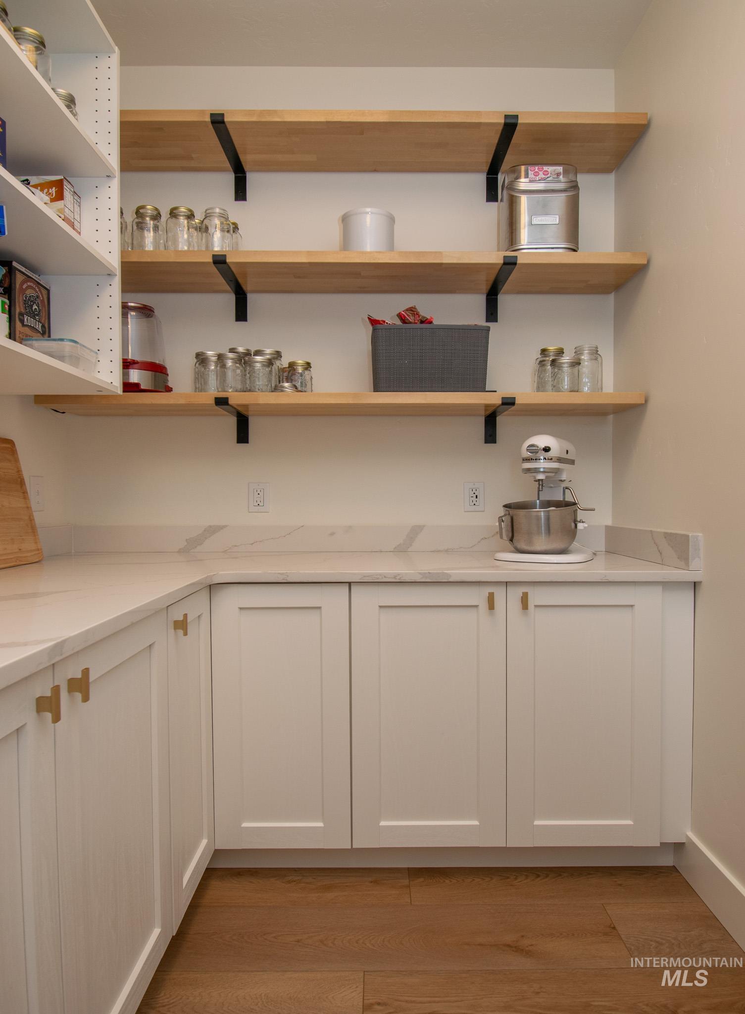 44 Big Moose Road McCall, ID 83638 - Photo 16 of 50 Custom pantry featuring open wood shelving with black metal supports, white shaker-style cabinetry, and light-toned countertops with a visible veining pattern