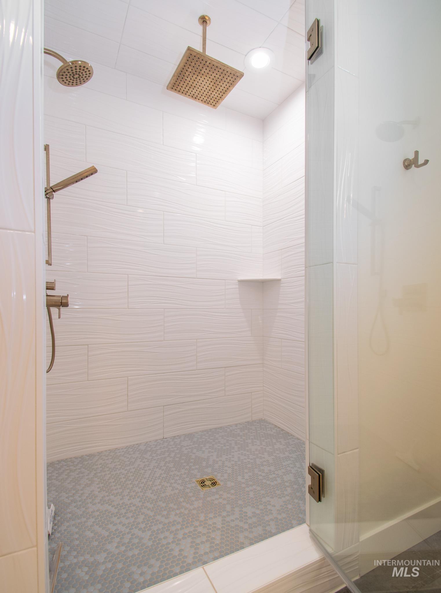 44 Big Moose Road McCall, ID 83638 - Photo 21 of 50 Walk-in shower featuring a dual shower system with a rain shower head and handheld sprayer, textured white tile walls, a built-in corner shelf, and a mosaic tile floor