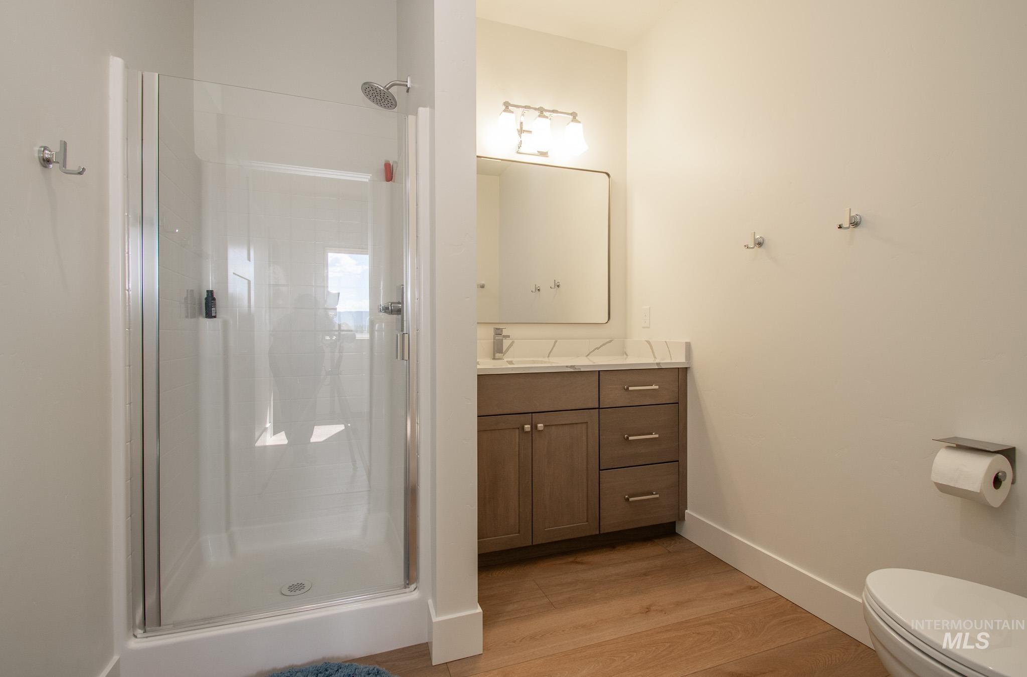 44 Big Moose Road McCall, ID 83638 - Photo 29 of 50 Contemporary bathroom featuring a glass-enclosed shower with a rainfall showerhead, a wood-finish vanity with a stone countertop and rectangular sink, and wood-finish flooring