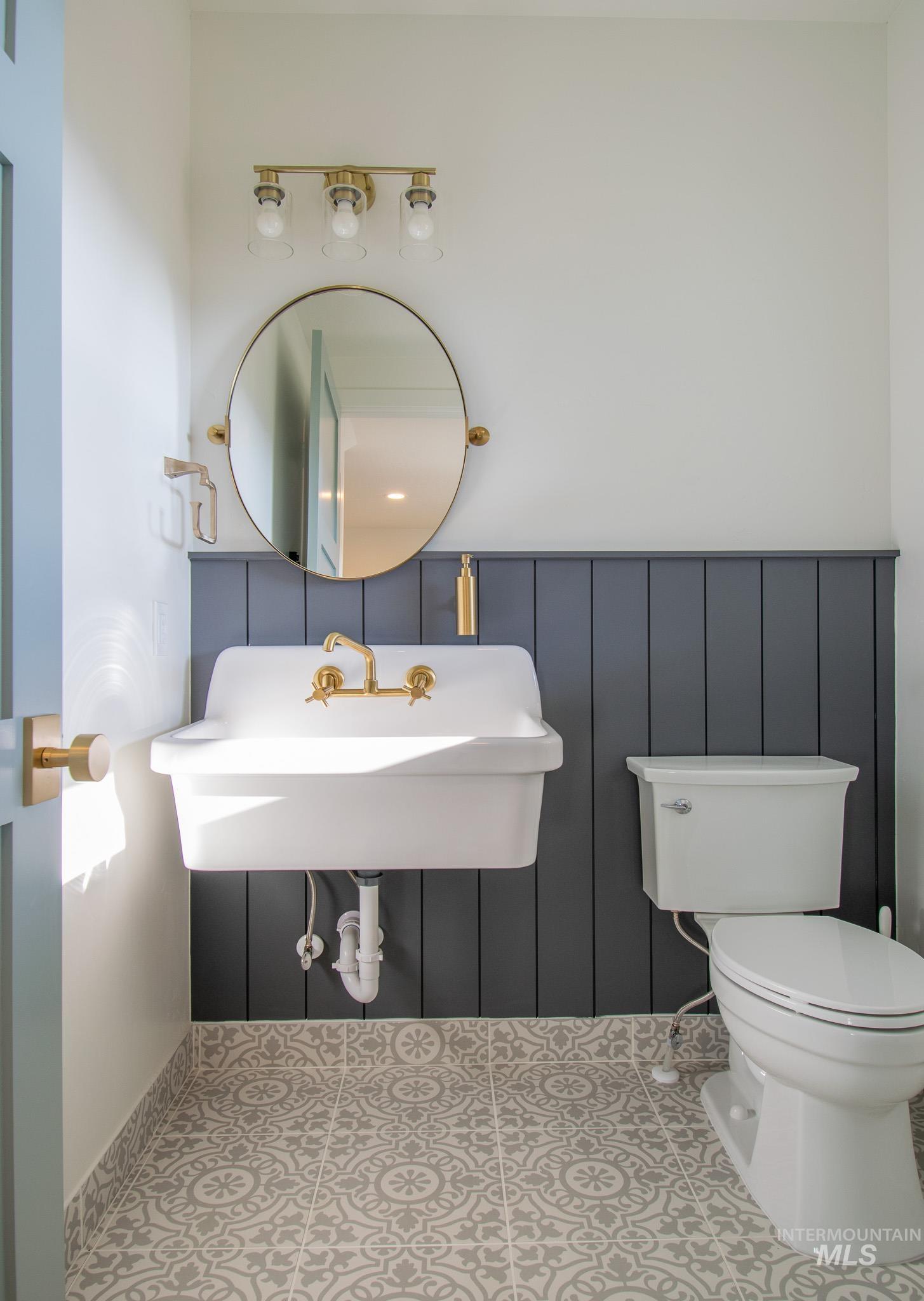 44 Big Moose Road McCall, ID 83638 - Photo 38 of 50 Bathroom featuring patterned floor tiles, dark gray wainscoting, a wall-mounted sink with brass fixtures, a coordinating brass framed mirror, and a three-light vanity fixture