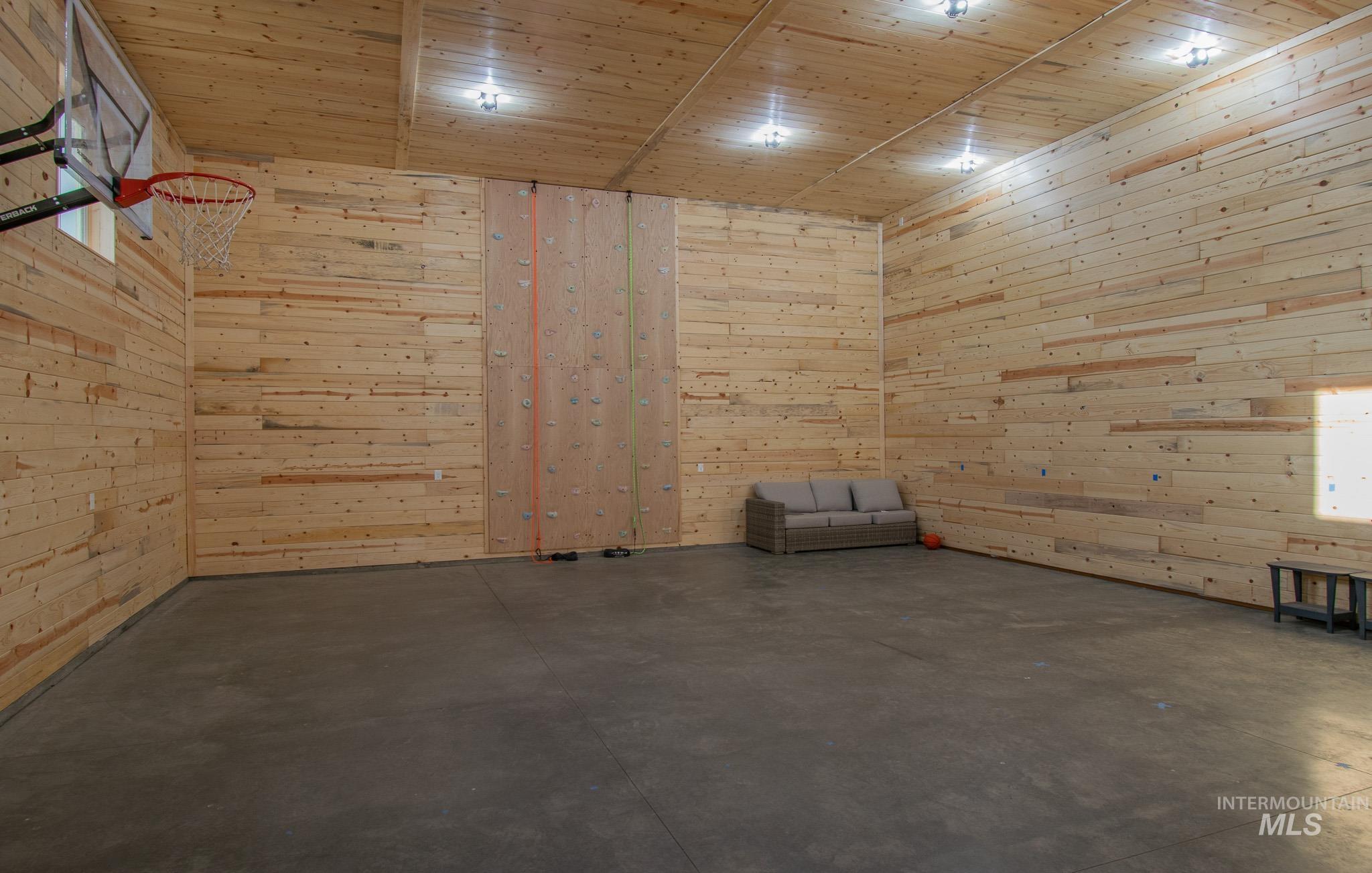 44 Big Moose Road McCall, ID 83638 - Photo 42 of 50 Spacious indoor recreational area featuring wood-paneled walls and ceiling, polished concrete flooring, a built-in climbing wall, a basketball hoop, and recessed lighting fixtures