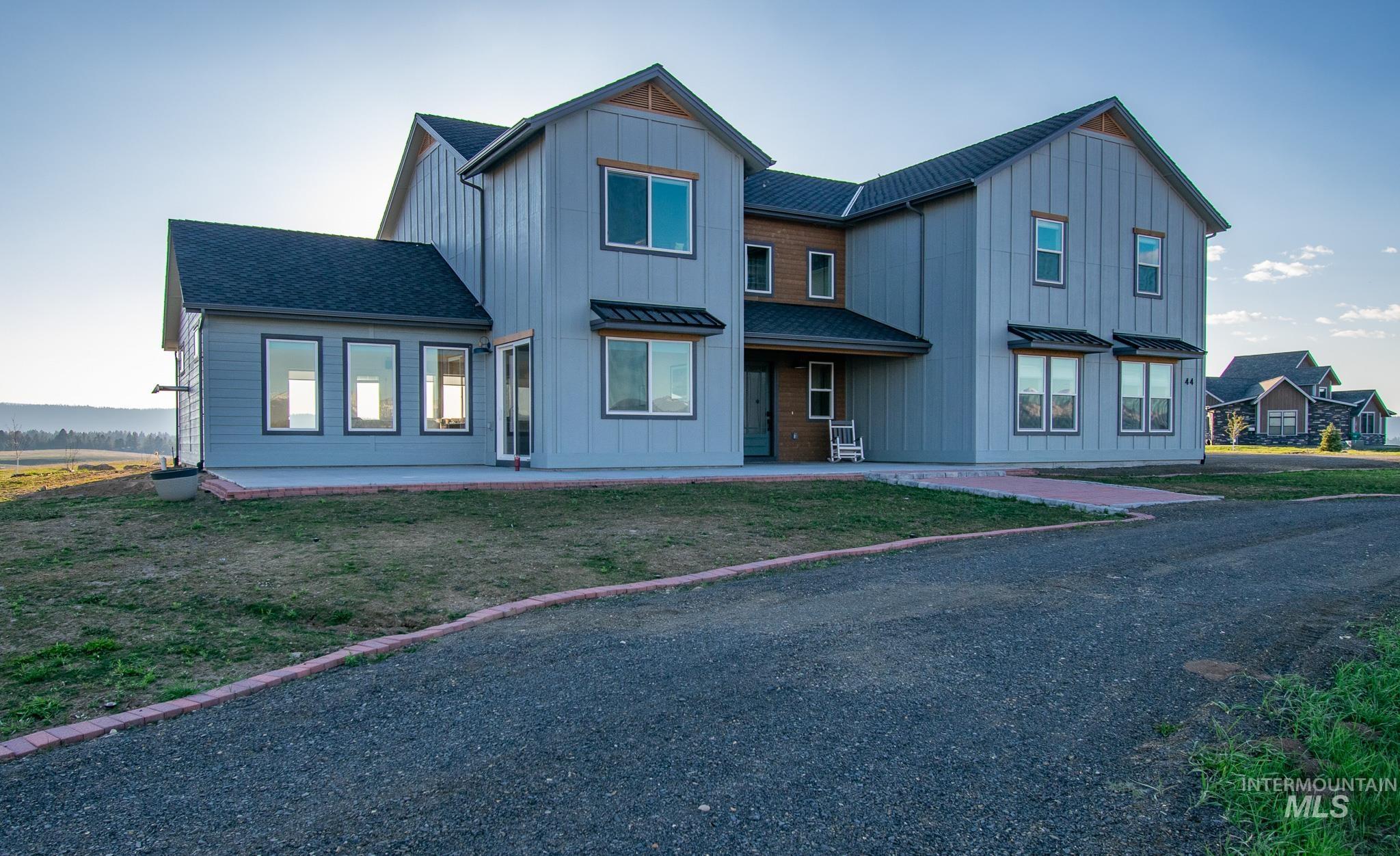 44 Big Moose Road McCall, ID 83638 - Photo 49 of 50 Modern farmhouse-style residence featuring vertical board and batten siding, dark shingle roofing, and a gravel driveway with brick edging