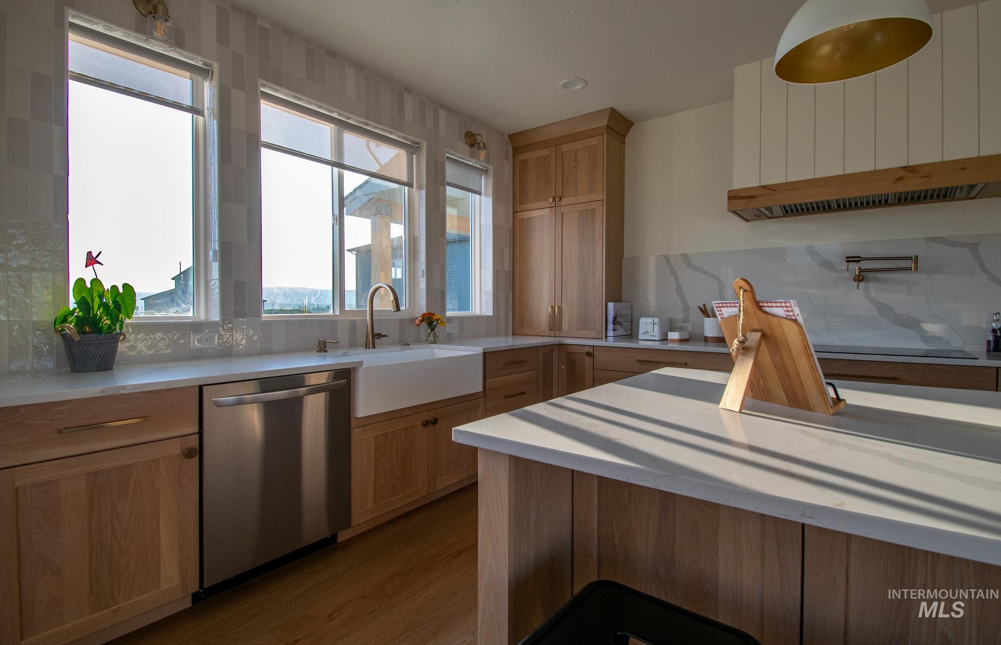 44 Big Moose Road McCall, ID 83638 - Photo 10 of 50 Modern kitchen featuring light wood cabinetry, a white farmhouse sink, stainless steel dishwasher, and a wall-mounted pot filler